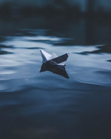 Paper boat floating on dark blue water